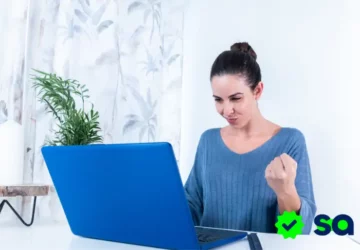 Mujer feliz frente a su computadora después de lograr ganar dinero trabajando desde casa.