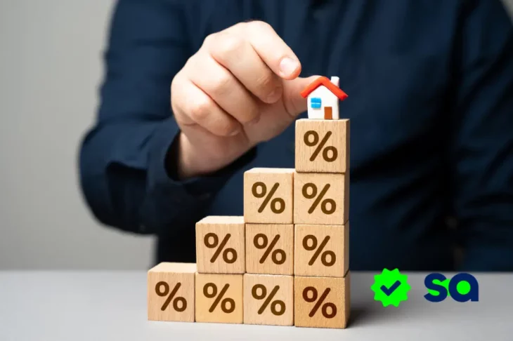 Persona colocando una casa en bloques de madera con signos de porcentaje