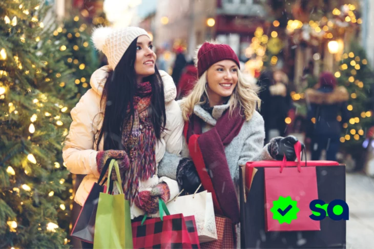 Dos mujeres con bolsas disfrutando de sus compras navideñas en una calle decorada