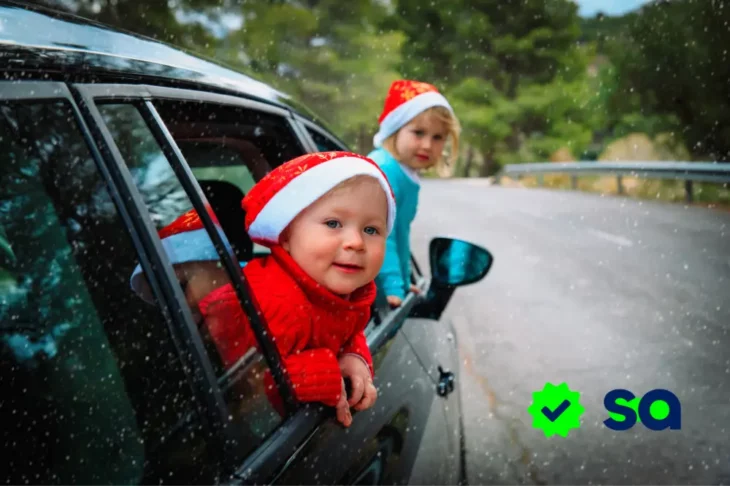 Niños con gorros navideños asomados por la ventana de un auto durante un viaje familiar