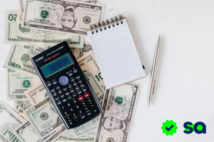 Calculadora, libreta y bolígrafo sobre una pila de billetes de dólar, simbolizando que el dinero bien gestionado te da libertad.