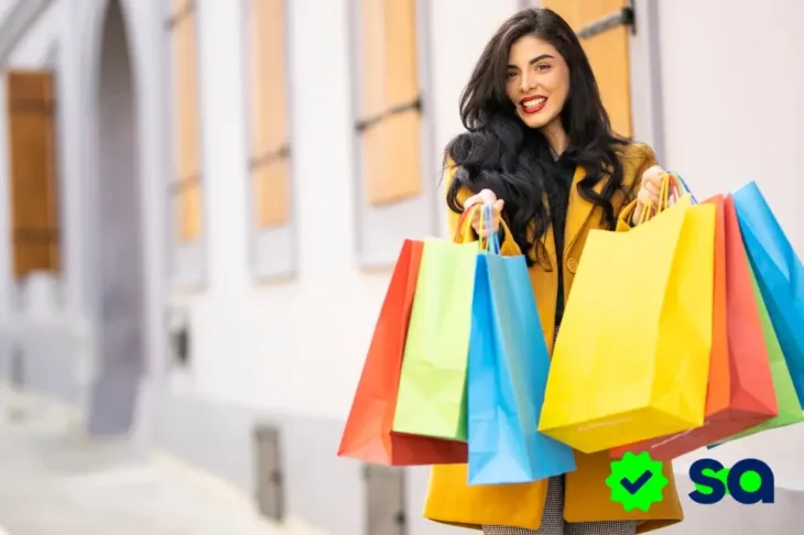 Mujer sonriente con varias bolsas de compras coloridas, representando el gasto impulsivo o gastar sin pensar.