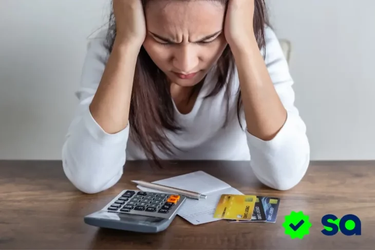 Mujer angustiada frente a facturas, tarjetas de crédito y una calculadora, representando el estrés por pagar deudas.
