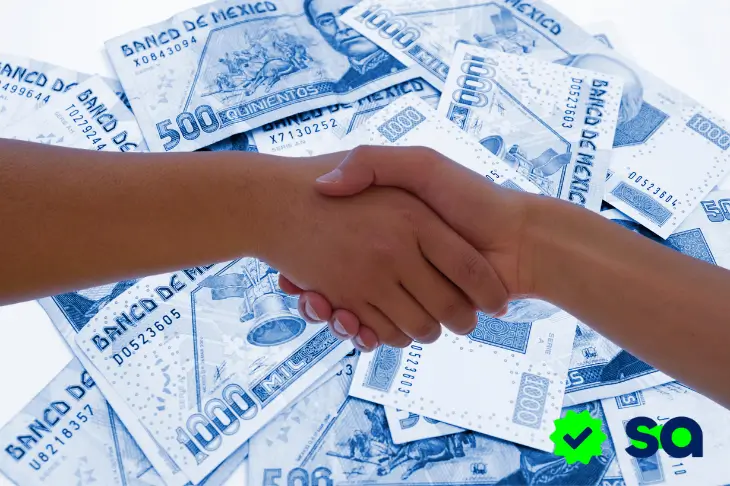Apretón de manos sobre billetes del Banco de México que simboliza un acuerdo de préstamos entre particulares.