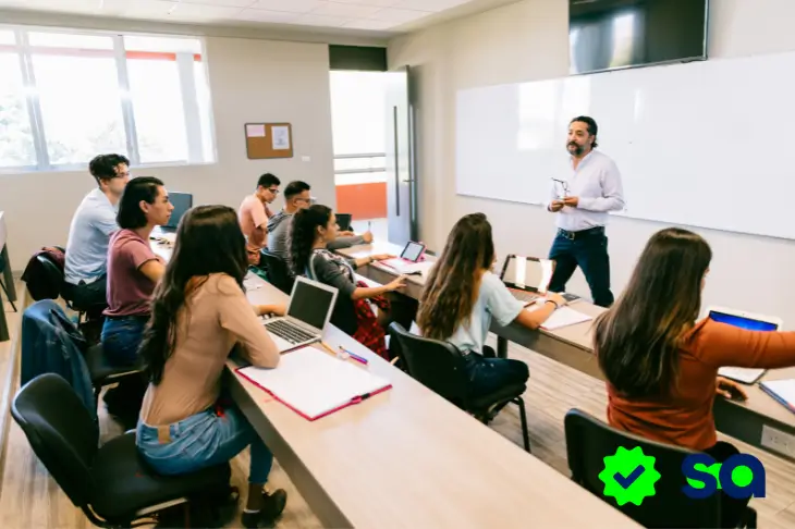 Estudiantes en un salón de clases escuchando al profesor, ilustrando el debate entre universidad pública vs universidad privada.