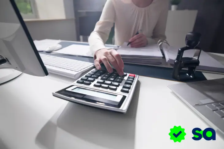 Persona usando una calculadora en la oficina para organizar finanzas y reducir gastos.