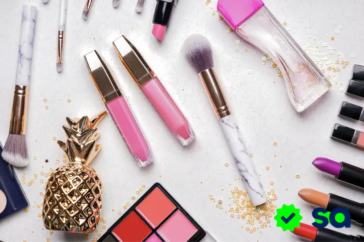 Muestras gratis, vista superior de cosméticos y brochas de maquillaje sobre una mesa clara.