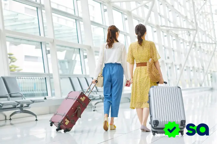 Viajeras caminando en un aeropuerto con maletas, imagen relacionada con seguro de viaje.