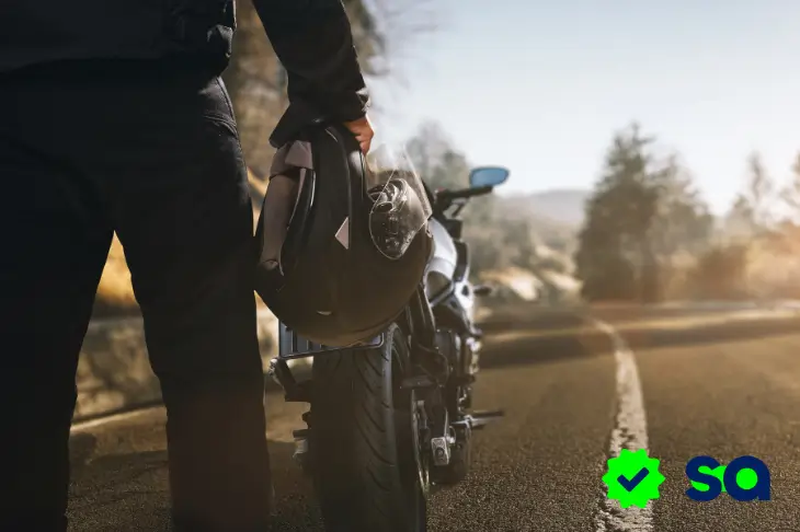 Persona sosteniendo un casco junto a una moto en carretera, imagen para contenido sobre seguro de motocicleta.