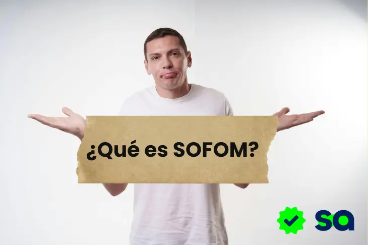 Hombre con gesto de duda sosteniendo un cartel que dice “¿Qué es SOFOM?”, sobre fondo blanco.