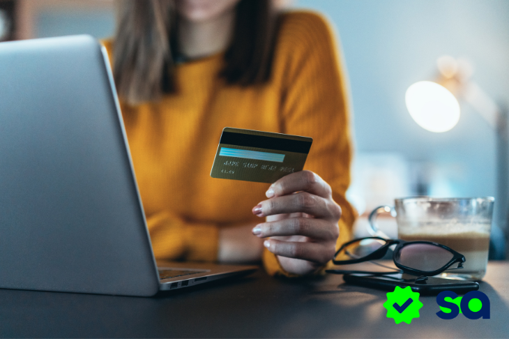Persona sosteniendo una tarjeta bancaria frente a una computadora portátil, imagen utilizada para ilustrar contenido sobre cargo no reconocido.