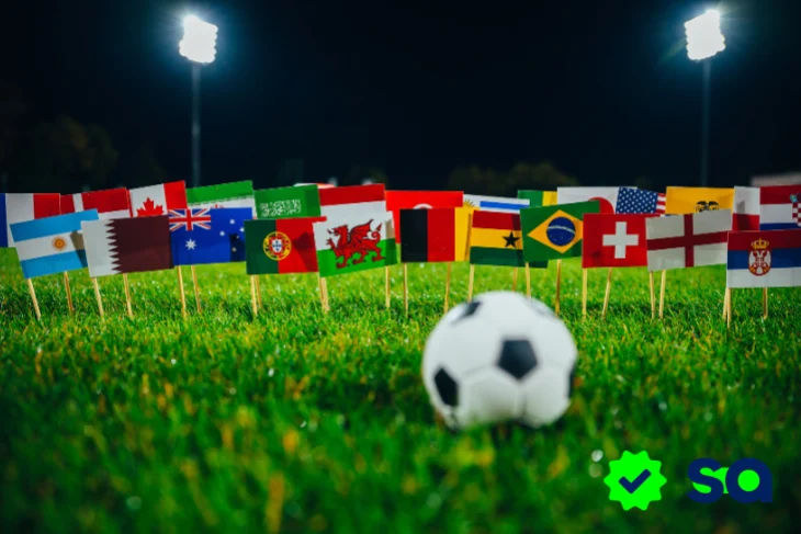 Banderas de diferentes países alrededor de un balón de fútbol en un estadio iluminado, representando la promoción Pásala para ganar rumbo al Mundial 2026™